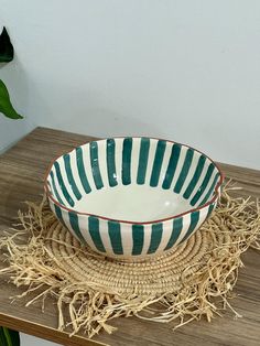 a green and white striped bowl sitting on top of a wooden table next to a potted plant