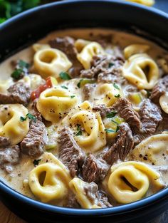 a blue bowl filled with pasta and beef in sauce on top of a wooden table