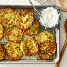 several crab cakes with sour cream and green onions on a baking sheet next to a bowl of sour cream