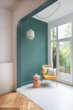 an empty room with a chair, lamp and large window in the corner that is painted teal