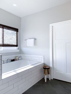 a white bath tub sitting under a window next to a wooden stool