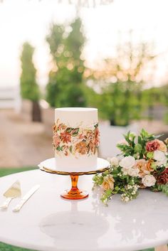 a wedding cake sitting on top of a white table next to flowers and silverware