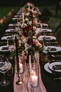 a long table is set with candles and plates for an elegant dinner party in the backyard