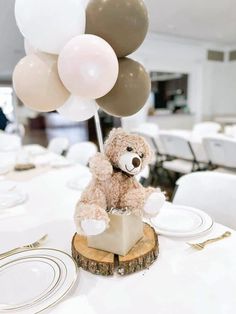 a teddy bear sitting on top of a wooden stump with balloons in the background at a party