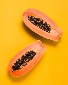 two halves of a papaya on a yellow background with black seed sprinkles