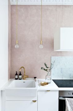 a white kitchen with pink walls and gold faucets hanging from the ceiling above it