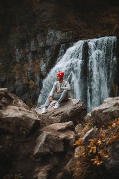 a man sitting on top of a rock next to a waterfall