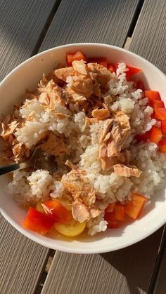 a bowl filled with rice and vegetables on top of a wooden table next to a fork