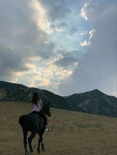 a woman riding on the back of a black horse across a dry grass covered field