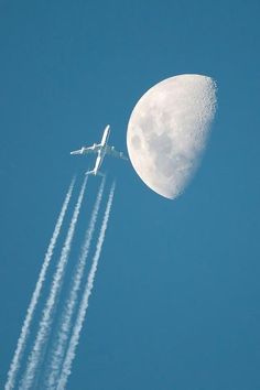 an airplane flying in the sky with a half moon behind it