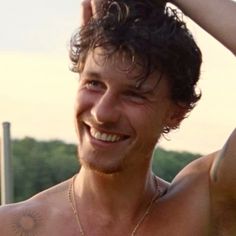 a man with no shirt on smiling and holding his hair in the air, wearing a necklace