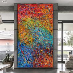 an abstract painting is hanging on the wall in a modern living room with large windows