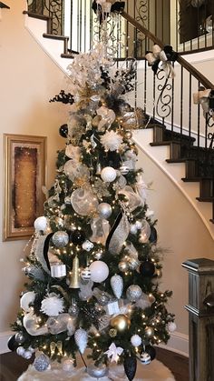 a decorated christmas tree with silver and white ornaments on it in front of a spiral staircase