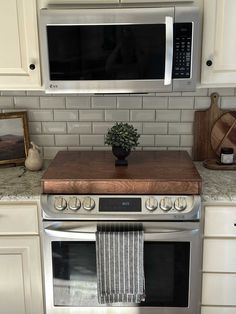 a potted plant sits on top of a wooden cutting board in front of an oven