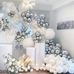 white and silver balloons are hanging from the ceiling in front of a table with flowers