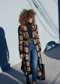 a woman with curly hair is walking down the street wearing jeans and a cardigan