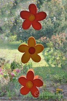 three red and yellow flowers are hanging in the air near some trees, grass and bushes