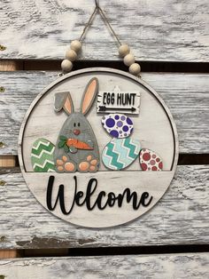 a welcome sign hanging on the side of a wooden fence with an egg hunt painted on it