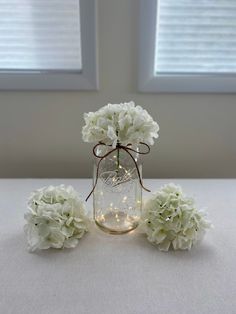 white hydrangeas in a mason jar with string lights on the side and two windows behind them