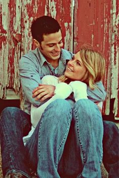 a man and woman sitting next to each other in front of a red barn door