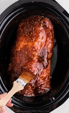 someone is using a brush to paint the meat in the slow cooker with red sauce