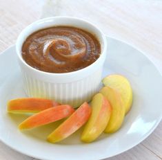 there is a small bowl of peanut butter next to sliced apples on a white plate