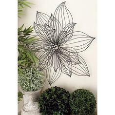 a metal wall decoration with a flower on it next to potted plants and greenery