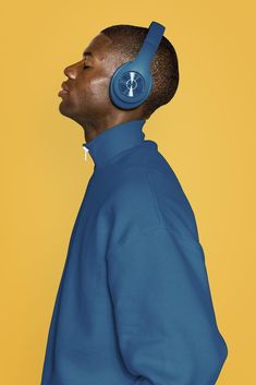 a man with headphones on his ears is looking to the side while standing against a yellow background