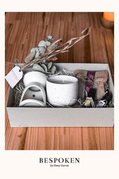 a box filled with white cups and saucers on top of a wooden table next to a candle