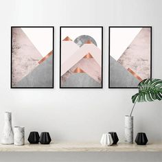 three framed art prints on a wall above a table with vases and plants in front of them