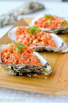 three open oysters on a wooden cutting board with red sauce and herbs in them