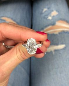 a woman's hand holding a diamond ring in front of her face and jeans on the floor