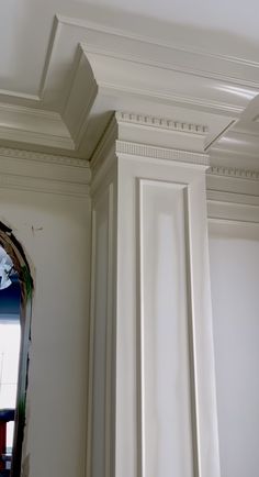 the corner of a room with white paint and molding on the walls, along with a mirror