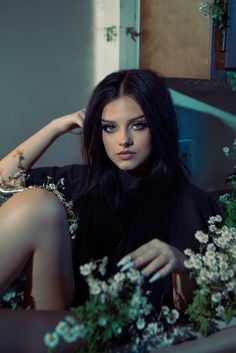 a woman sitting on the ground with flowers in her hand and looking at the camera