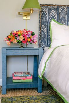 a blue nightstand with flowers and books on it next to a white bedspread