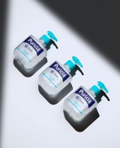 three hand sanitizers sitting on top of a white table next to each other