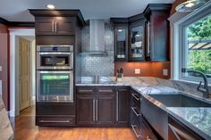 a kitchen with dark wood cabinets and marble counter tops, along with stainless steel appliances