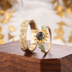 two gold rings sitting on top of a wooden table next to another ring with a black diamond in the middle