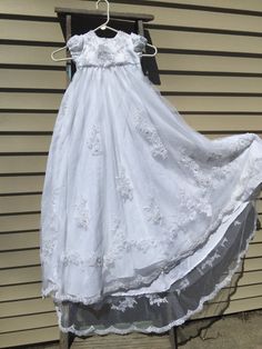 a white dress hanging on a clothesline outside in front of a house with a hanger