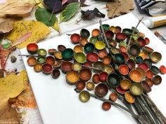 a white cutting board topped with lots of different types of paintbrushes on top of leaves