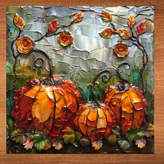 two pumpkins sitting on top of a wooden table next to leaves and flowers in front of a stained glass window