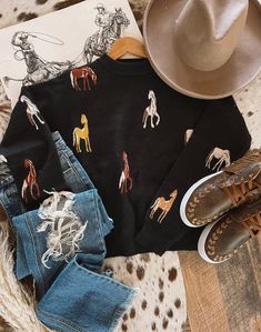 a cowboy hat, jeans and boots are on top of a cow print sweater that has horses all over it