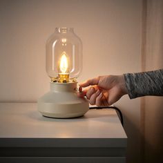 a person's hand holding a light bulb on top of a small white table