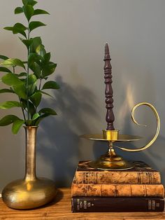 two books and a candle are on a table next to a vase with a plant in it