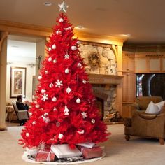 a red christmas tree with white snowflakes on it in front of a fireplace