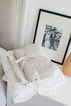 a stack of folded linens sitting on top of a white table next to a vase