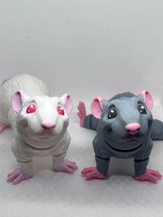 three toy mice sitting next to each other on a white tablecloth covered surface, one with pink eyes and the other grey