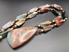 This lovely necklace showcases an exquisite Ocean Jasper pendant in enchanting hues of red, green, gray, and brown. The necklace is elegantly complemented by 10 to 20 mm figural Ocean Jasper beads, along with high-quality misty Quartz faceted beads and Czech fire-polished beads. The necklace is elegantly secured with a gold-plated hook clasp, guaranteeing both durability and style. Necklace length: 26 inches/67 cm. Pendant measures 58 by 35 mm/2,3 in by 1,4 in.  Indulge in the beauty of nature a Jasper Gemstone Beaded Necklaces As Gift, Jasper Gemstone Beaded Necklace As Gift, Multicolor Jasper Jewelry For Gift, Multicolor Jasper Necklace For Gift, Elegant Jasper Necklace For Gift, Handmade Multicolor Jasper Jewelry, Elegant Jasper Beaded Necklace For Gift, Unique Multicolor Jasper Necklaces, Quartz Pendant Necklace