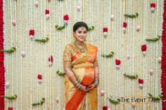 a woman standing in front of a wall with flowers and beads on the wall behind her