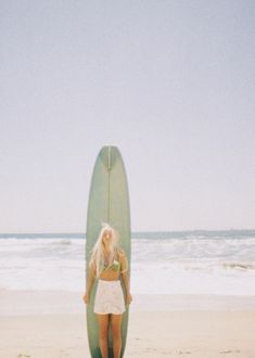 a woman standing on the beach with her surfboard in front of her head and body